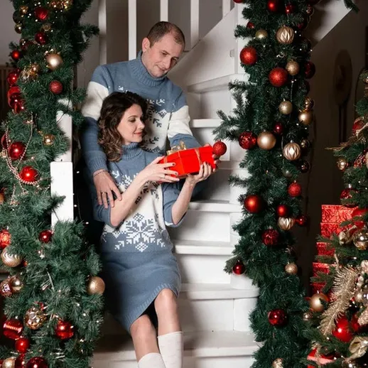 Пара на лестнице, радостно открывающая подарок в рождественском убранстве дома