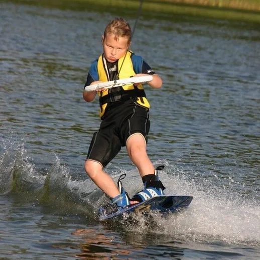 Мальчик катается на водных лыжах на озере в ясный солнечный день, демонстрируя свои навыки и чувство равновесия
