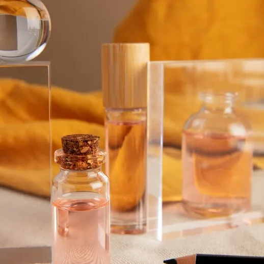 Элегантные флаконы с духами и прозрачные подставки на фоне желтой ткани в светлом интерьере