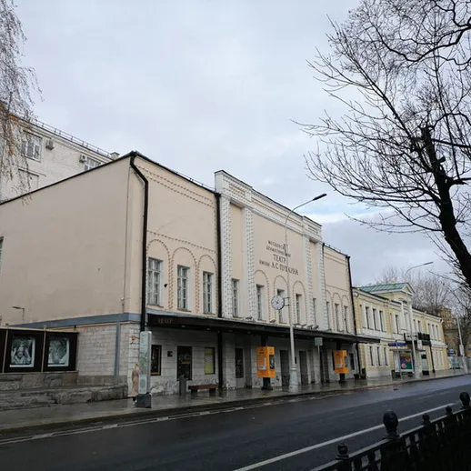 Здание театра на улице в Москве в серый осенний день с листопадом и пустой проезжей частью