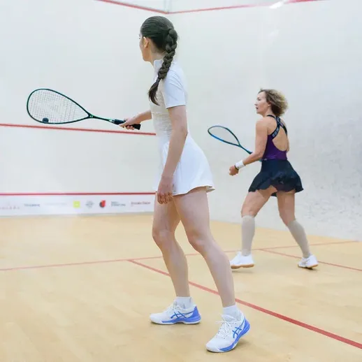 Две спортсменки играют в сквош в закрытом зале в белой и темной форме