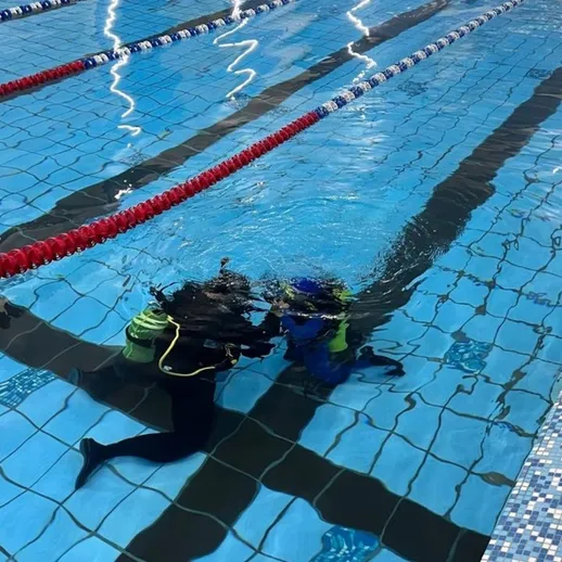 Урок подводного плавания, проводимый инструктором для ученика в бассейне в вечернее время