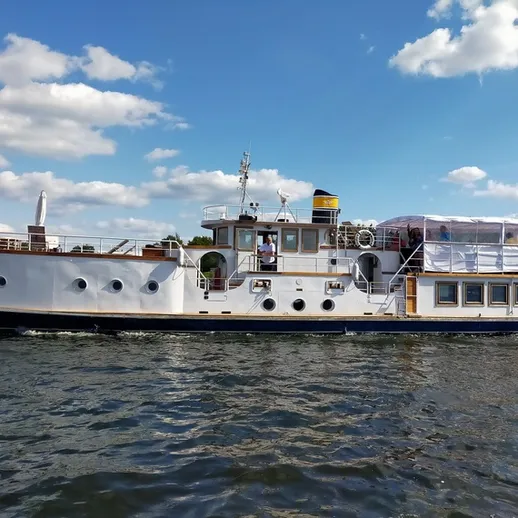 На реке находится старинный пароход, плывущий под голубым небом с облаками в летний день