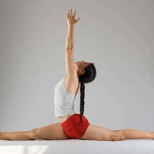 Женщина выполняет растяжку на сцене с нейтральным фоном, демонстрируя гибкость и силу в профессиональной спортивной форме