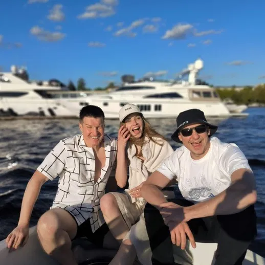 Трое людей на лодке на фоне яхт на воде в ясный день