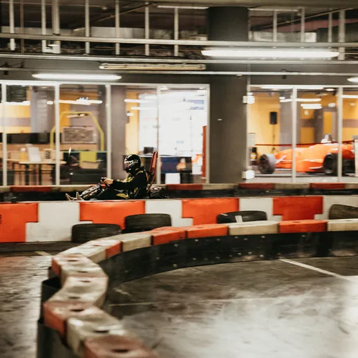 Заезд в картинг-центре: гонщик на трассе в многолюдном помещении в вечернее время