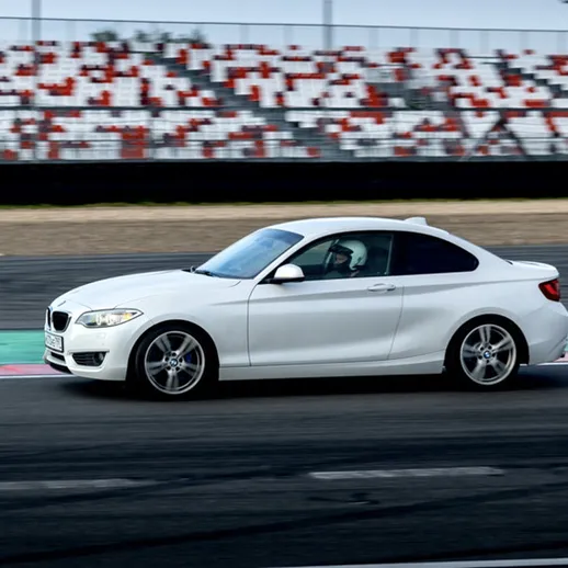 Белый спорткар на автодроме во время гонки, яркий день, зрители на трибунах наблюдают за происходящим