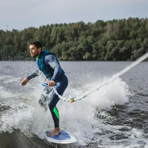 Серфинг на озере, молодой человек катается на доске с буксировкой в ясный солнечный день