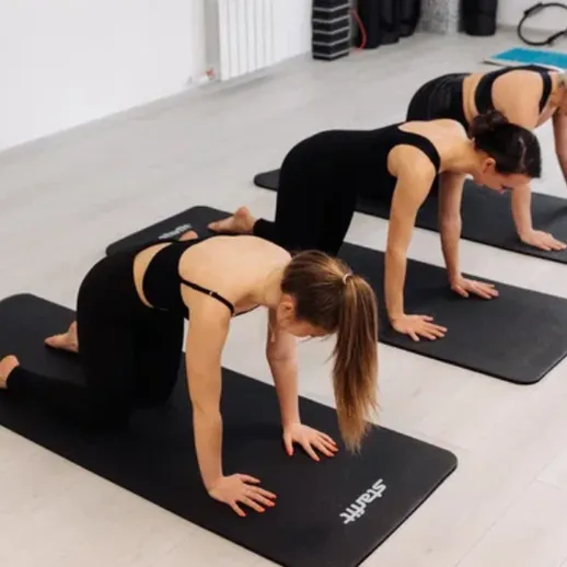 Три женщины занимаются йогой в фитнес-зале в утренние часы, практикуя позы на ковриках для занятий