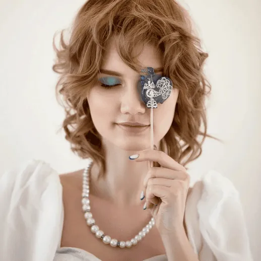 Молодая женщина в свадебном платье с мейкапом, прикрывающая один глаз украшенной палочкой