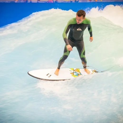 Сёрфер на искусственной волне в аквапарке, занятие серфингом в теплом климате