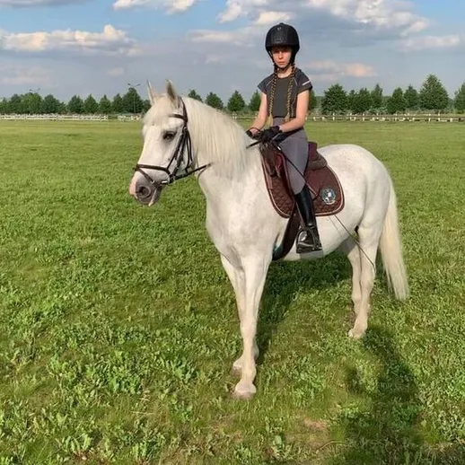 Девочка верхом на белом коне на зелёном поле в солнечный день