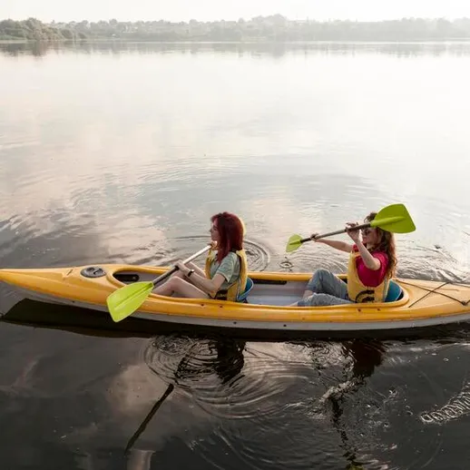 Две девушки гребут на желтой байдарке по спокойной воде на реке в ясный день