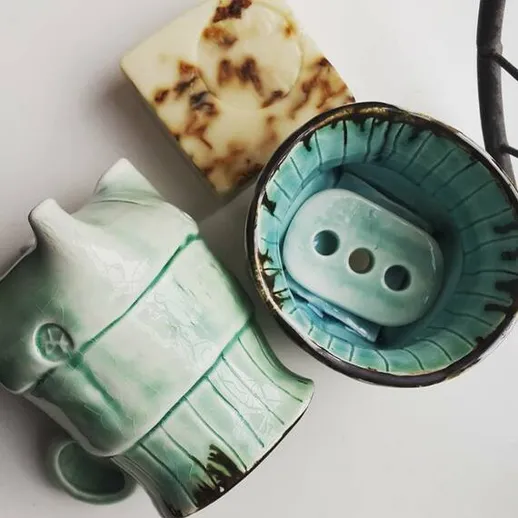 Керамические предметы с голубой отделкой на белом фоне, включая чашу, мыльницу и мыло, размещенные в уютной композиции