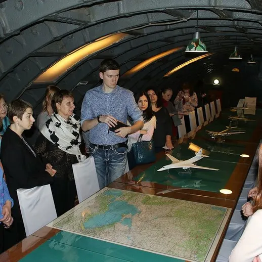 Группа людей обсуждает планы на конференции в подземном помещении с картой и моделями самолетов