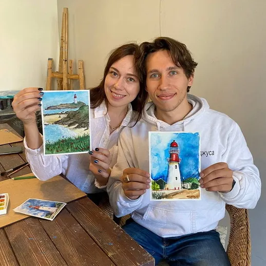 Молодая пара демонстрирует акварельные картины маяка и побережья в уютной мастерской