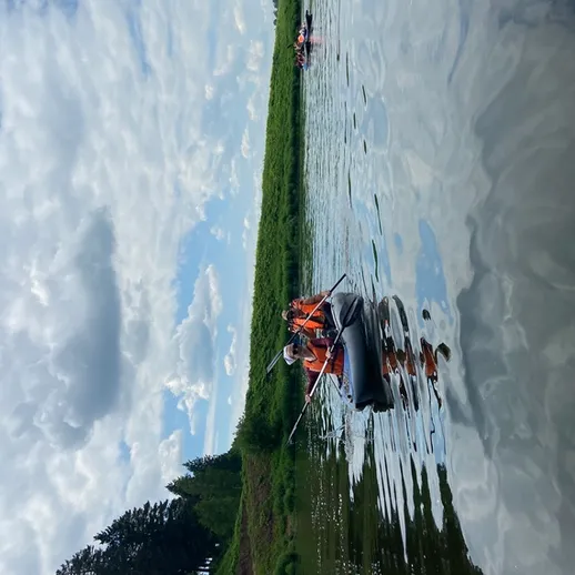 Плавание на резиновом катамаране по спокойной реке в ясный день в окружении зелёных холмов и облачного неба