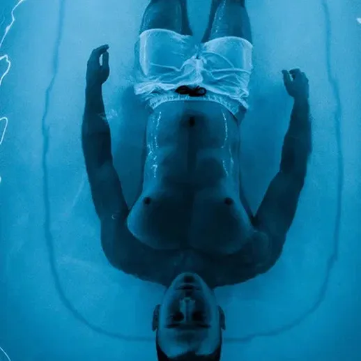 Мужчина плавает в воде в светлом бассейне в ночное время