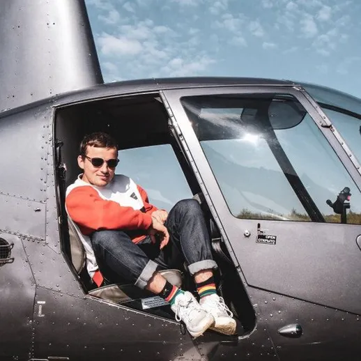 Мужчина сидит в открытой двери вертолета на фоне ясного неба и природы