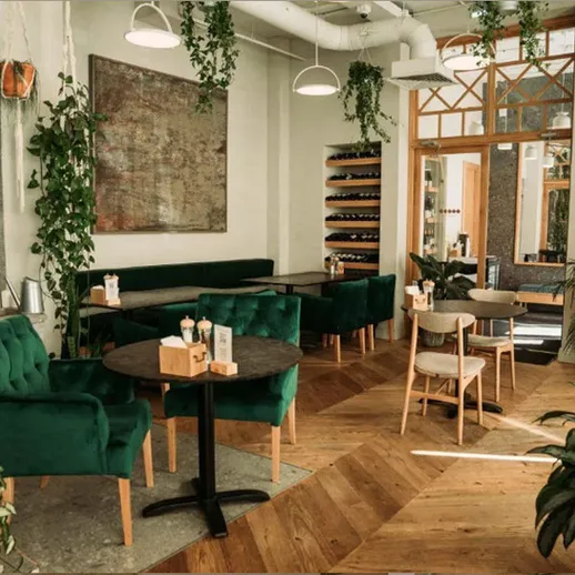 Уютное кафе с зелеными растениями и стильной мебелью в центре города, идеальное для отдыха и встреч с друзьями