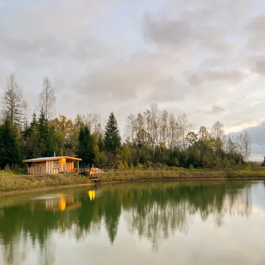 Уютный домик на берегу озера в осенний день с отражением в воде и облачным небом