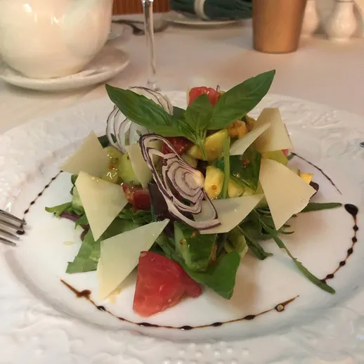 Свежий салат с авокадо и пармезаном на белой тарелке в уютном ресторане