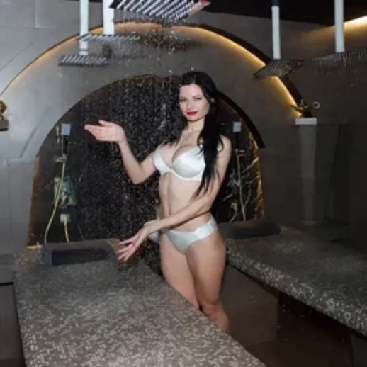 Женщина в купальнике наслаждается водопадом в спа-салоне в вечернее время