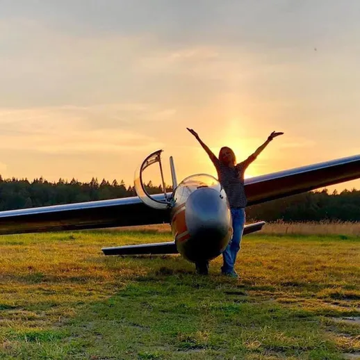 Девушка радуется на фоне планера на закате в лесистой местности