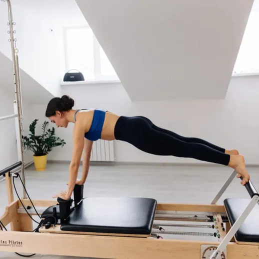 Женщина занимается пилатесом на тренажере в светлом зале с окнами в солнечный день