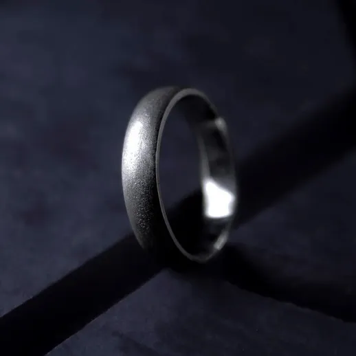 Крупный план металлического кольца на темной поверхности, создающий атмосферу загадочности и элегантности в ночном свете