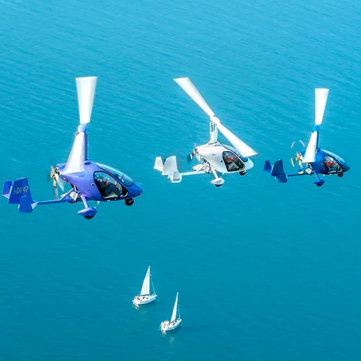 Трёхместные вертолёты над спокойной водой с парусными лодками внизу в ясный день