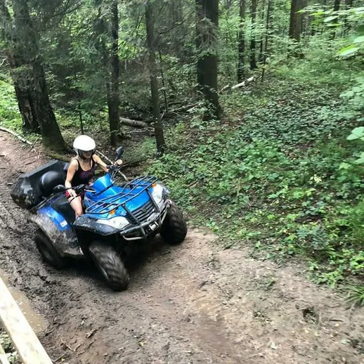 Человек на квадроцикле совершает поездку по пересеченной местности в лесу в летний день