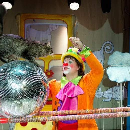 Клоун взаимодействует с кошкой на арене цирка во время представления