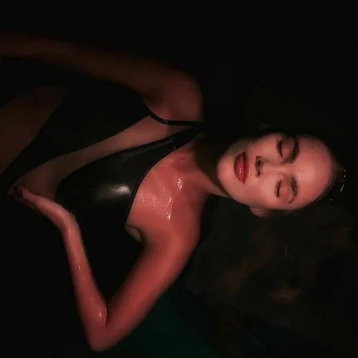 Женщина в черной купальнике плавает в темной воде, освещенной мягким светом в вечернее время