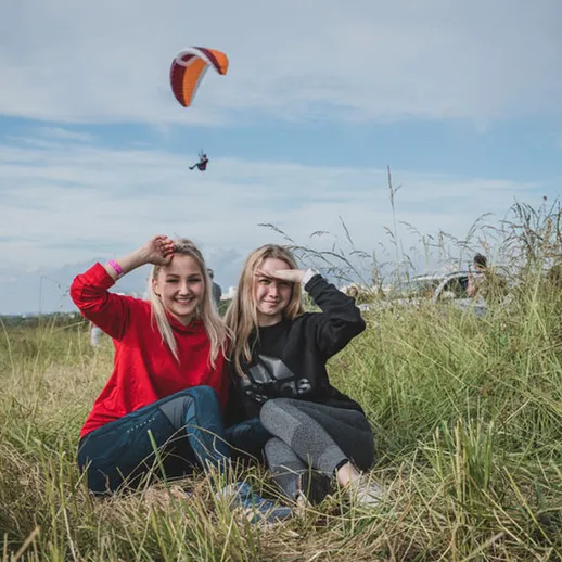 Два человека веселятся на природе, наслаждаясь днем на открытом воздухе, рядом с парапланом и зелеными лугами