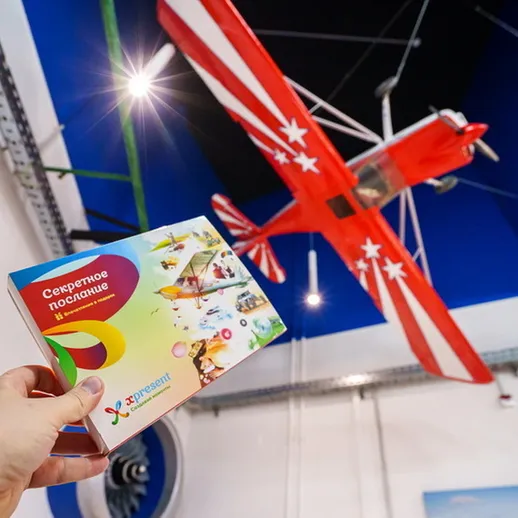 Ручка держит открытку с секретным посланием на фоне красного модели самолета в выставочном центре