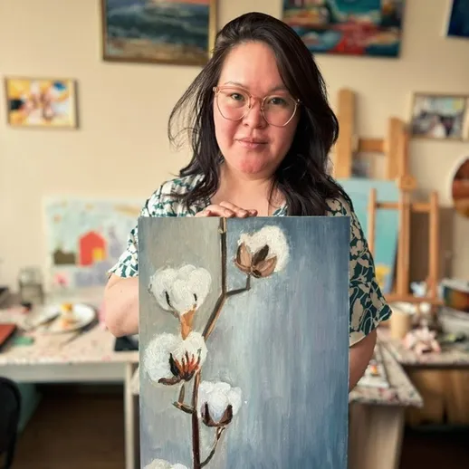 Художница демонстрирует свою картину с цветами хлопка в мастерской