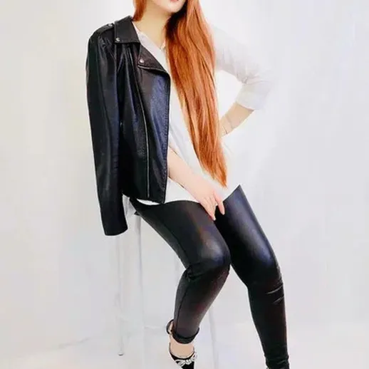 Молодая женщина с длинными волосами и кожаной курткой позирует на стуле в студии