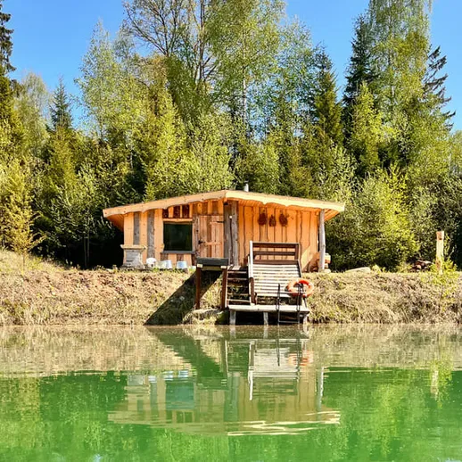 Уютный домик на берегу озера в лесу, окруженный зелеными деревьями, в солнечный весенний день