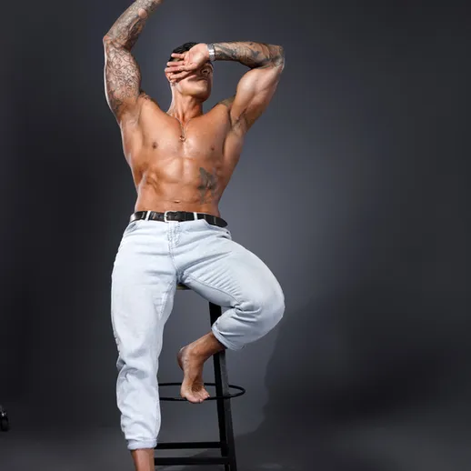 Мужчина с татуировками позирует на табурете в студии с нейтральным фоном