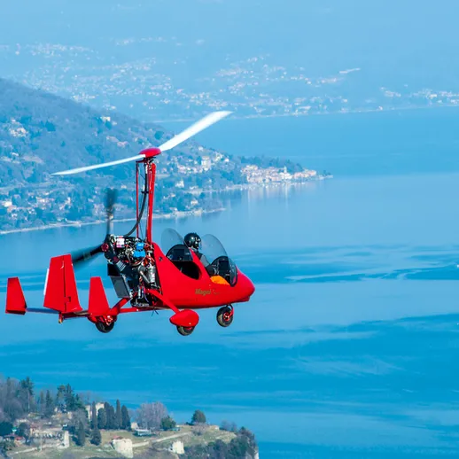 Красный легкий самолет с мощным пропеллером летит над живописным озером в ясный солнечный день