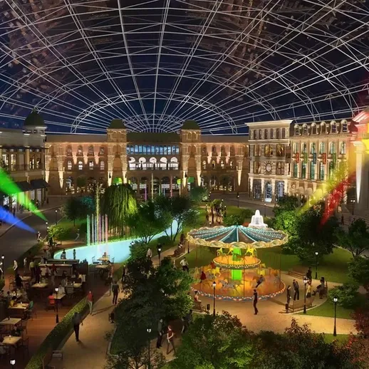 Многолюдная площадь с фонтаном и аттракционами ночью в современном торговом центре