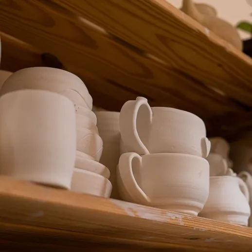 Глиняные чаши и посуда на полке в мастерской керамики, выполненные вручную, на фоне светлого дерева