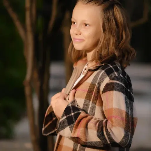 Улыбающаяся девочка в клетчатой кофте на фоне тёмного сада вечером