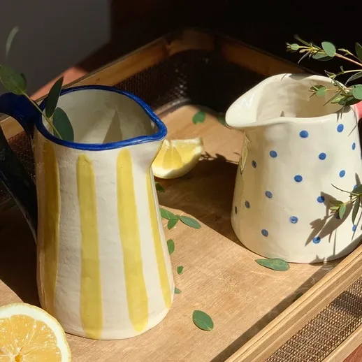 Керамические кувшины с лимоном и зелеными ветками на деревянном подносе в уютном интерьере