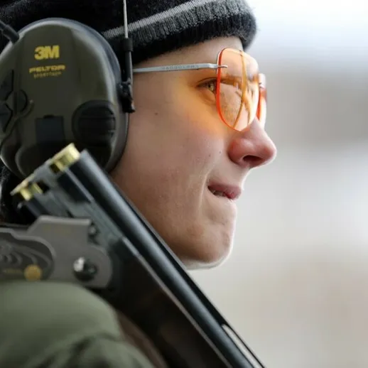 Молодой стрелок в защитных наушниках и очках на стрельбище в зимний день