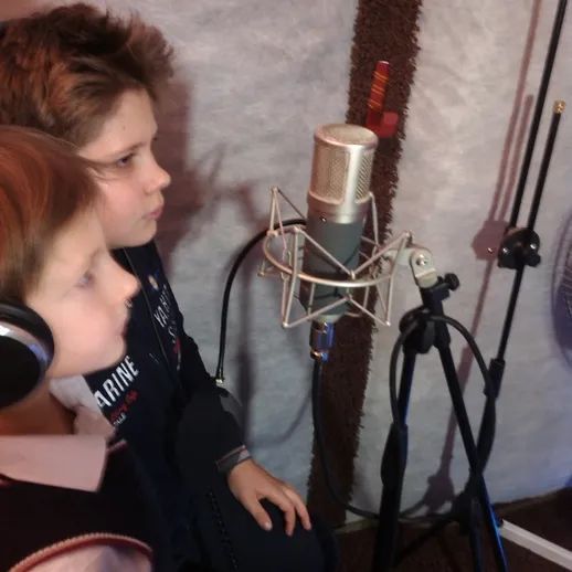 Дети записывают песню в студии звукозаписи с микрофоном на фоне звукоизолирующих панелей