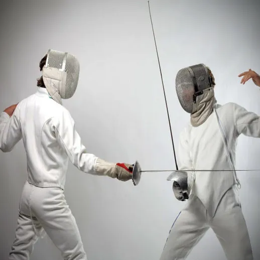 Два спортсмена по фехтованию соревнуются на тренировке в закрытом помещении в вечернее время