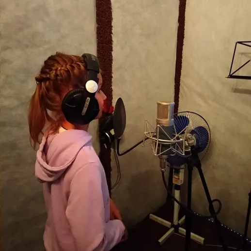 Девушка поет в студии звукозаписи, окруженная профессиональным оборудованием и микрофоном