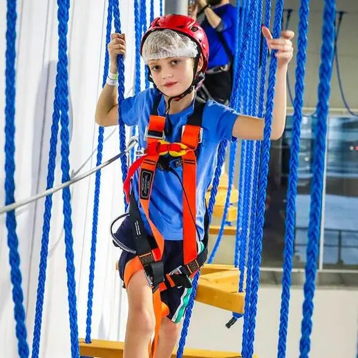 Мальчик в защитной экипировке преодолевает препятствия на веревочном курсе в закрытом помещении